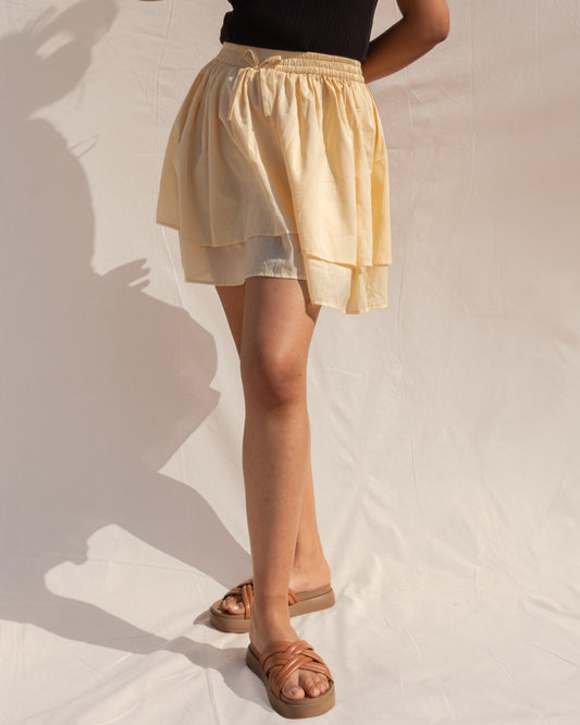 Woman wearing a black top and yellow skirt against a neutral background