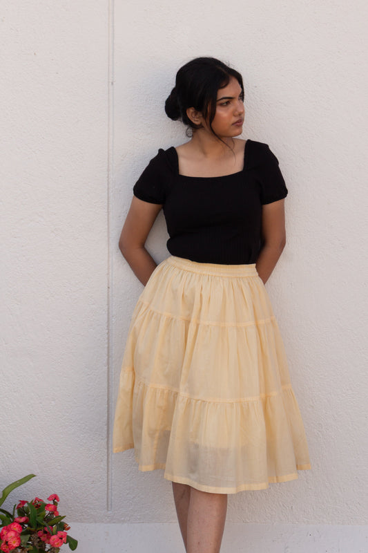 Woman wearing a black top and beige skirt against a white wall