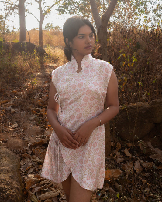 Woman in a floral dress standing in a natural setting with trees and rocks.
