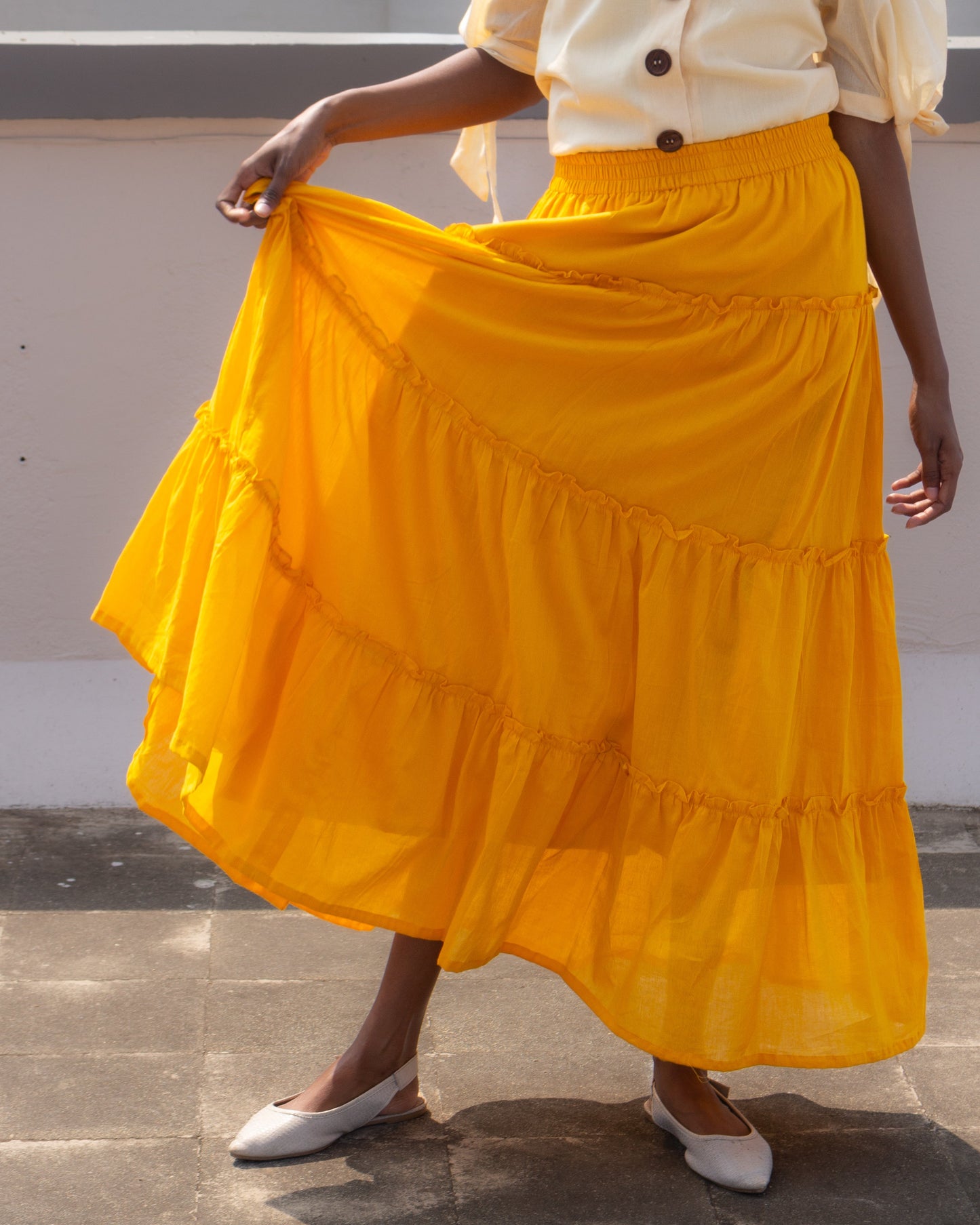 Person wearing a yellow tiered skirt and white blouse on a neutral background