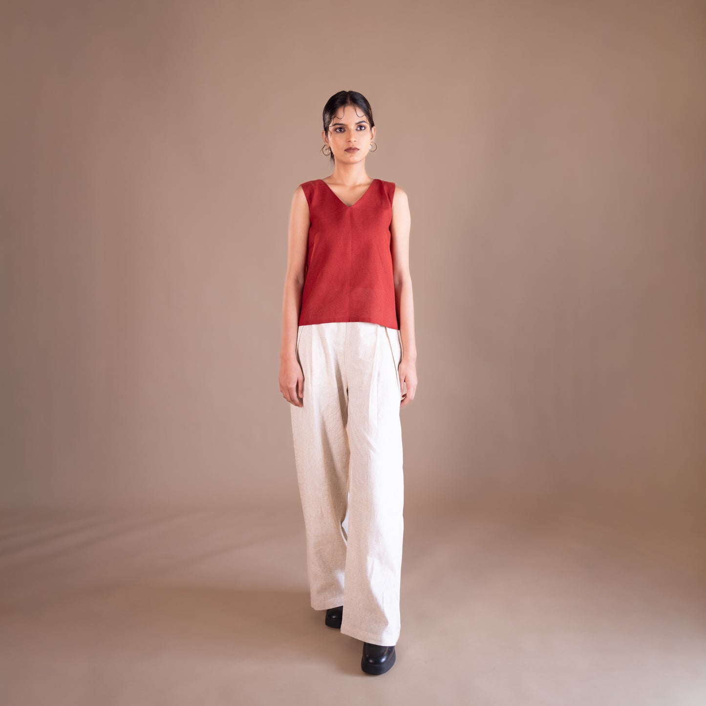 Woman wearing a red sleeveless top and beige pants against a brown background