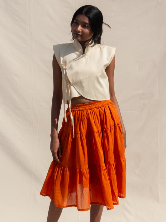 Woman wearing a white top and orange skirt against a plain background