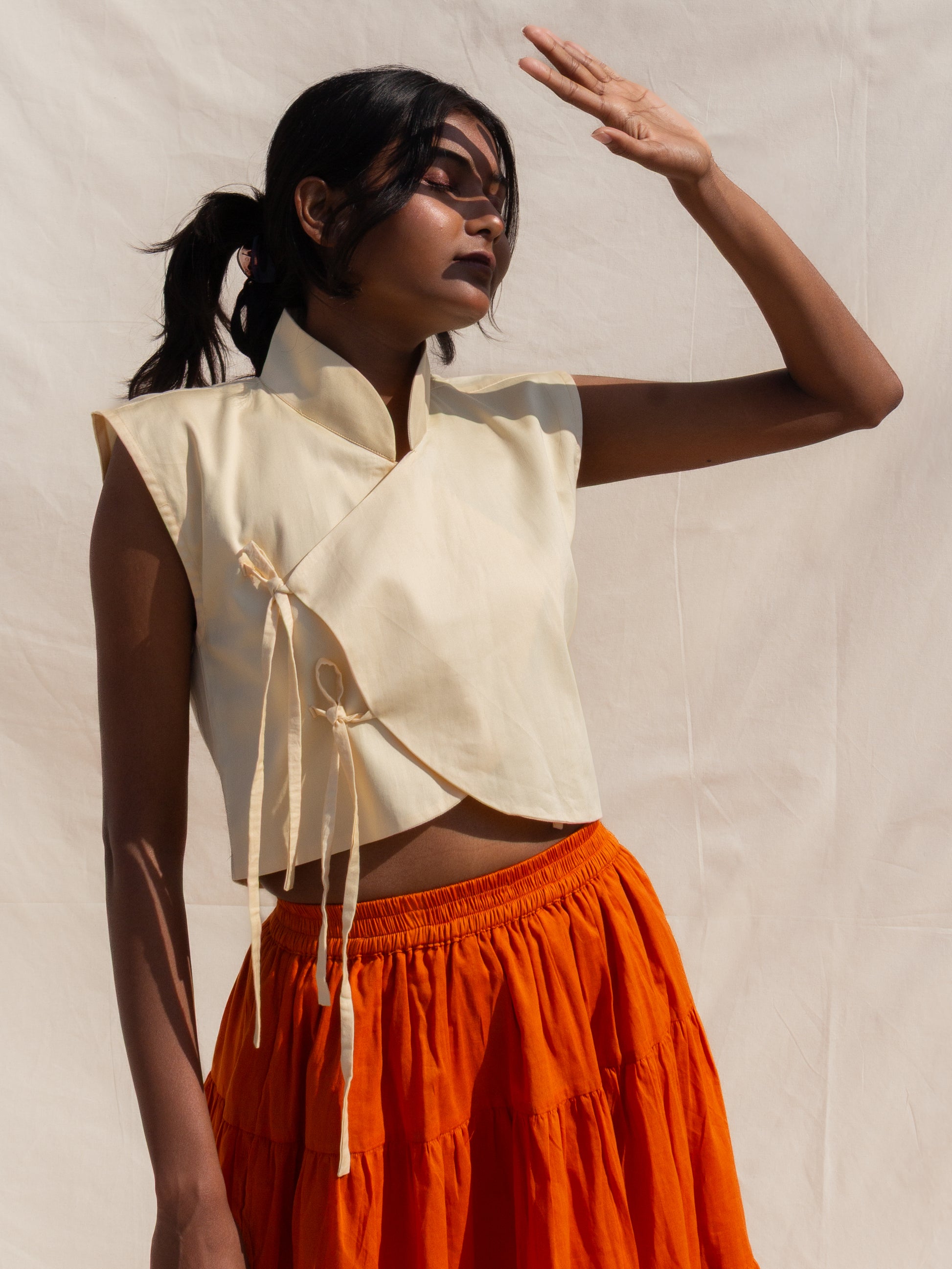Woman wearing a beige sleeveless top and orange skirt against a plain background