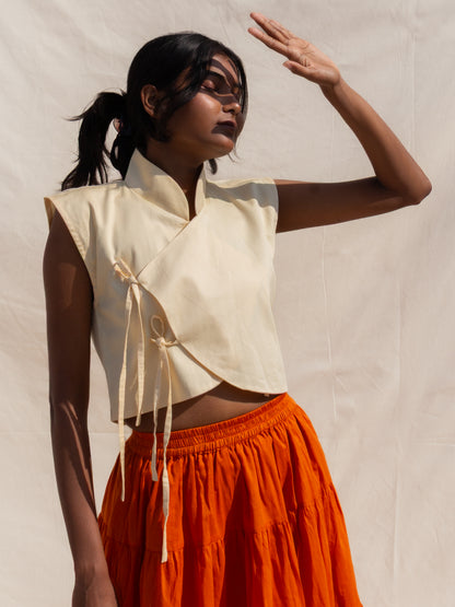 Woman wearing a beige sleeveless top and orange skirt against a plain background