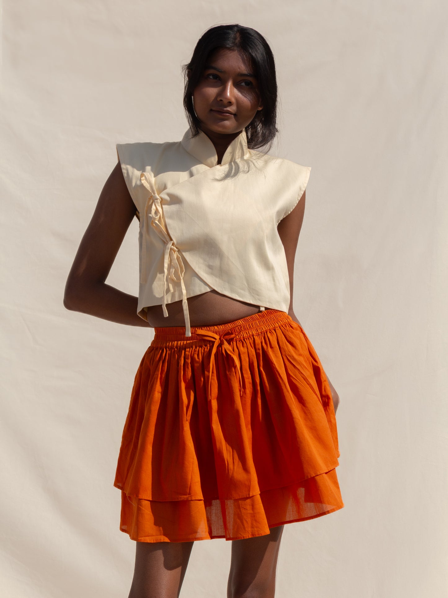 Woman wearing a white top and orange skirt against a plain background