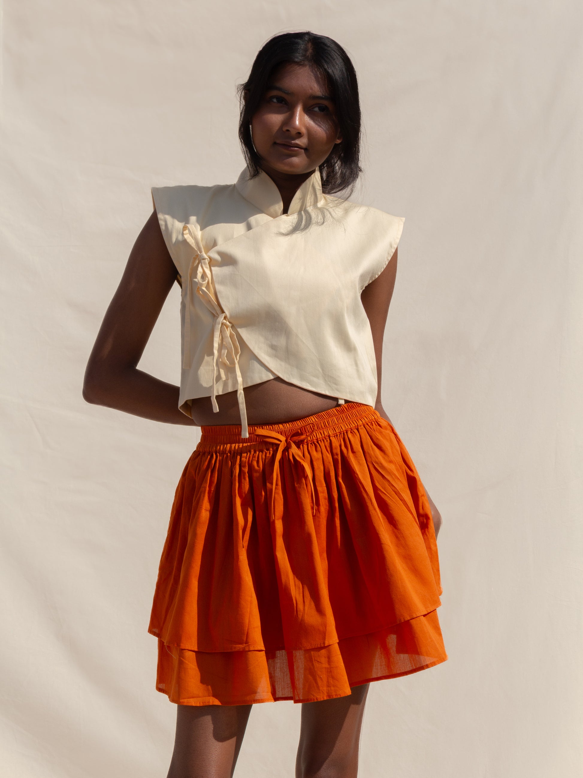 Woman wearing a white top and orange skirt against a plain background