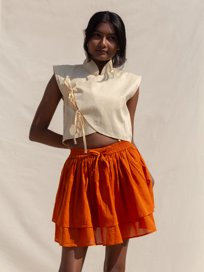 Woman wearing a white top and orange skirt against a plain background