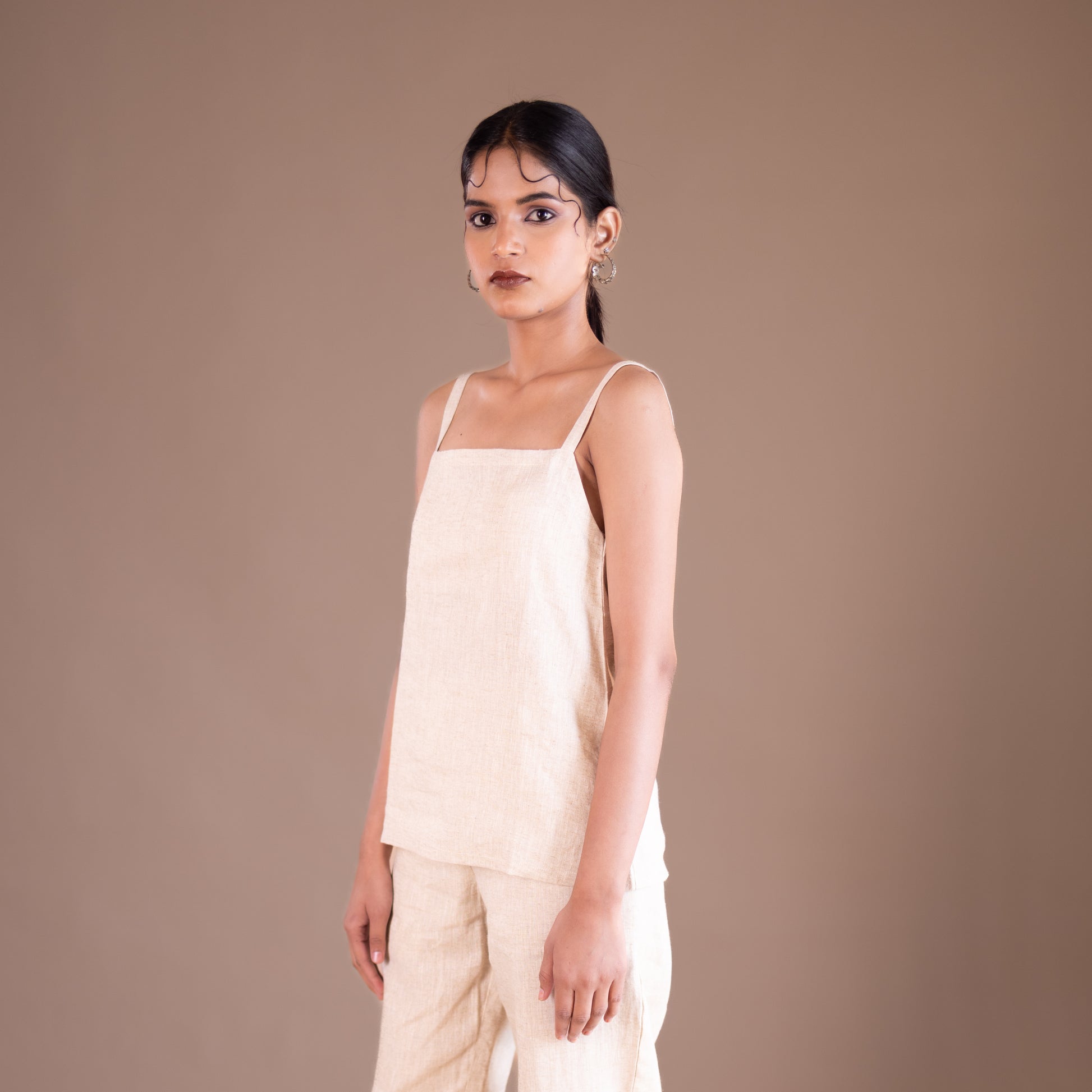 Woman wearing a beige sleeveless top and pants against a brown background