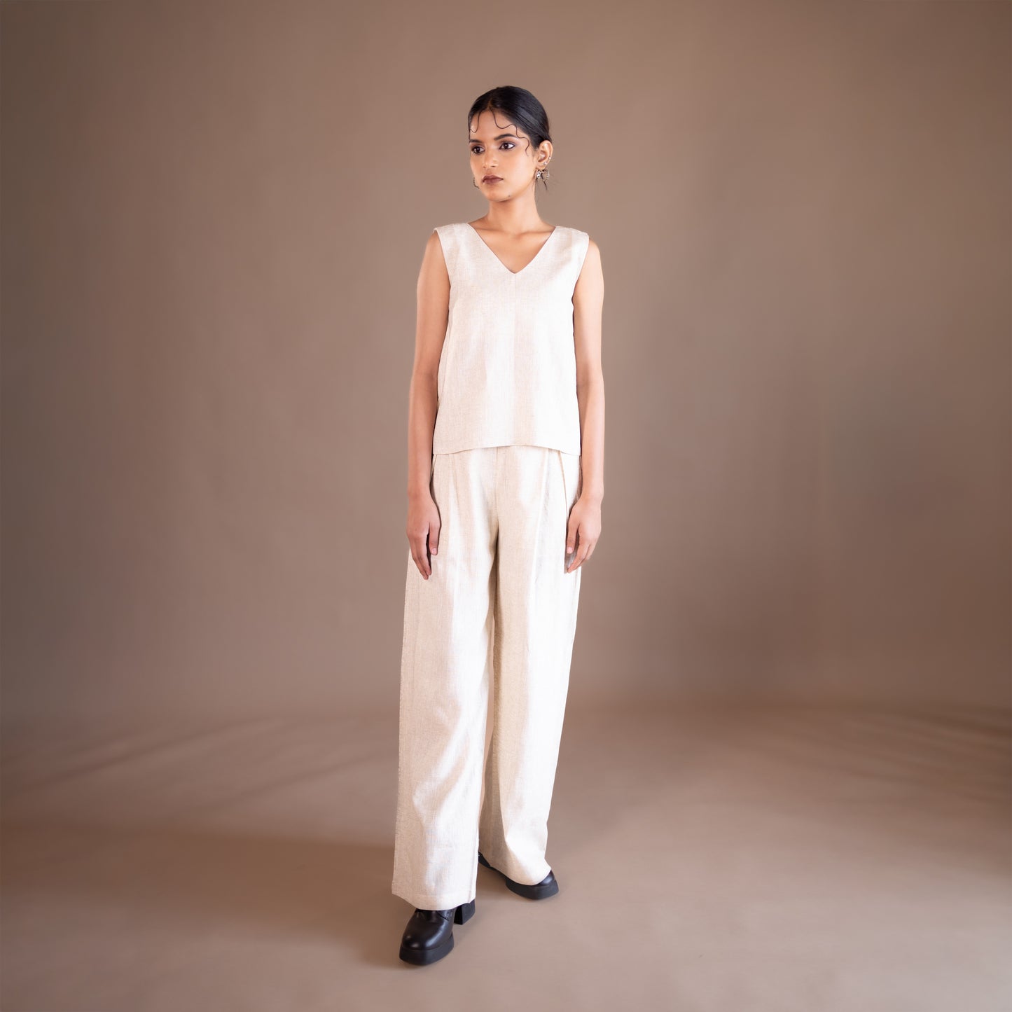Woman wearing a beige jumpsuit against a brown background