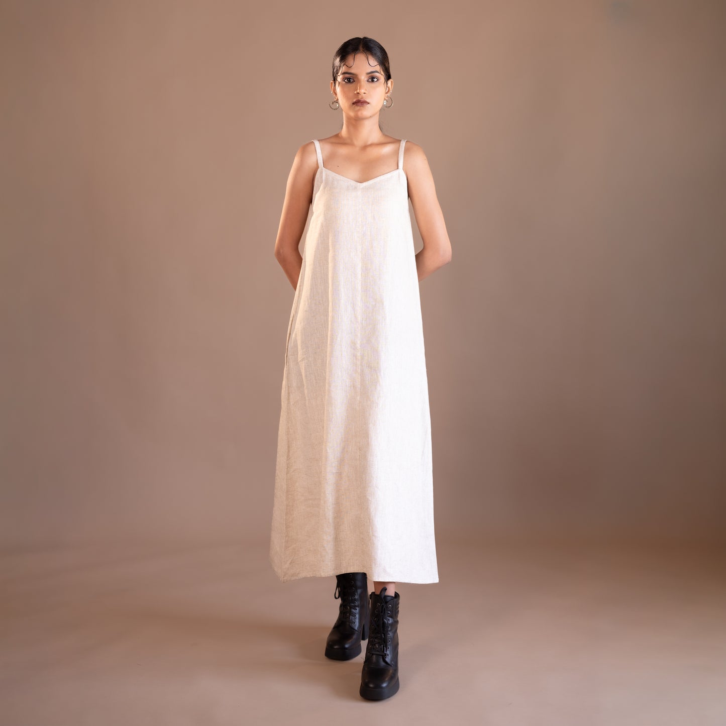 Woman wearing a beige dress with black boots on a brown background