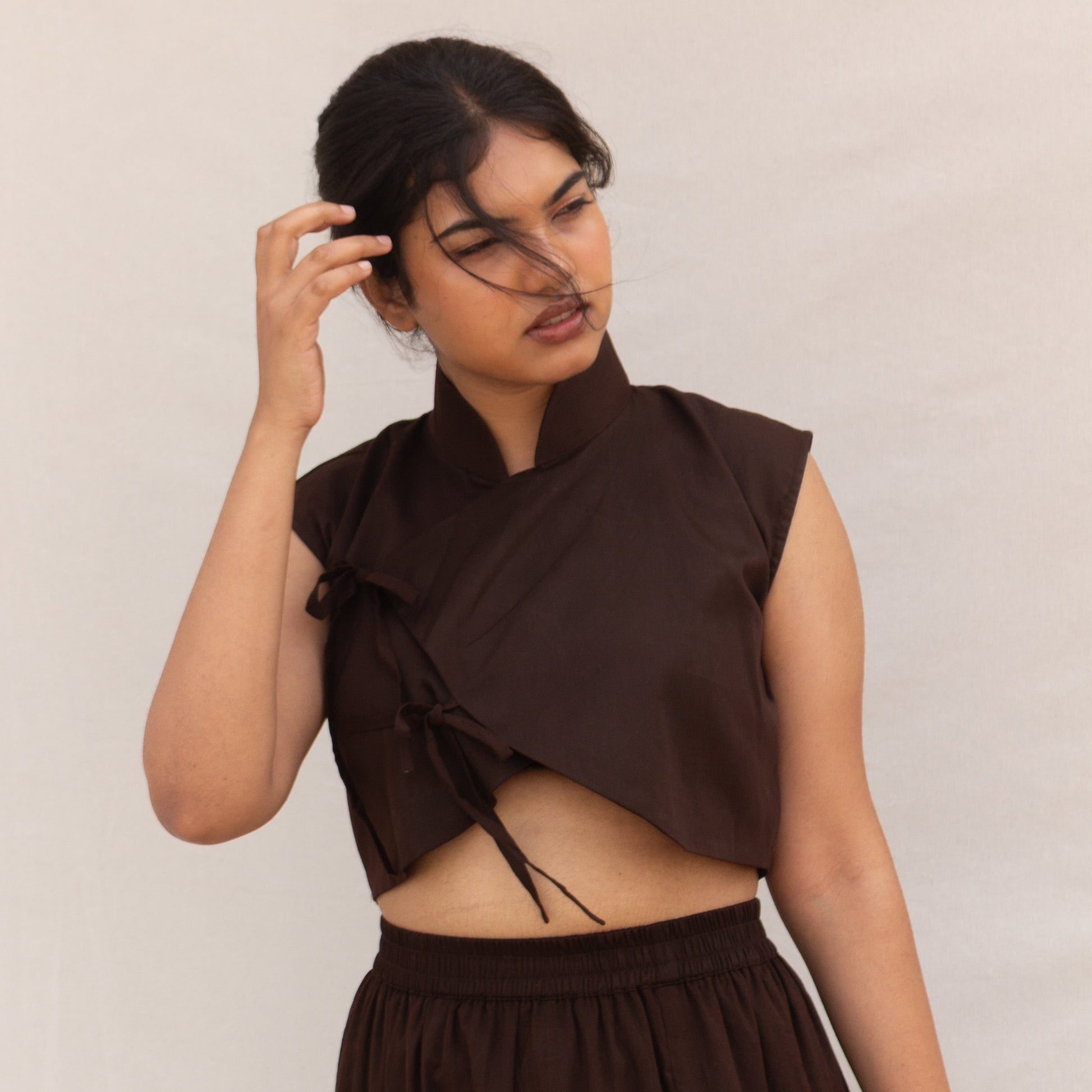 Woman wearing a brown sleeveless top with cut-out design and matching skirt against a plain background