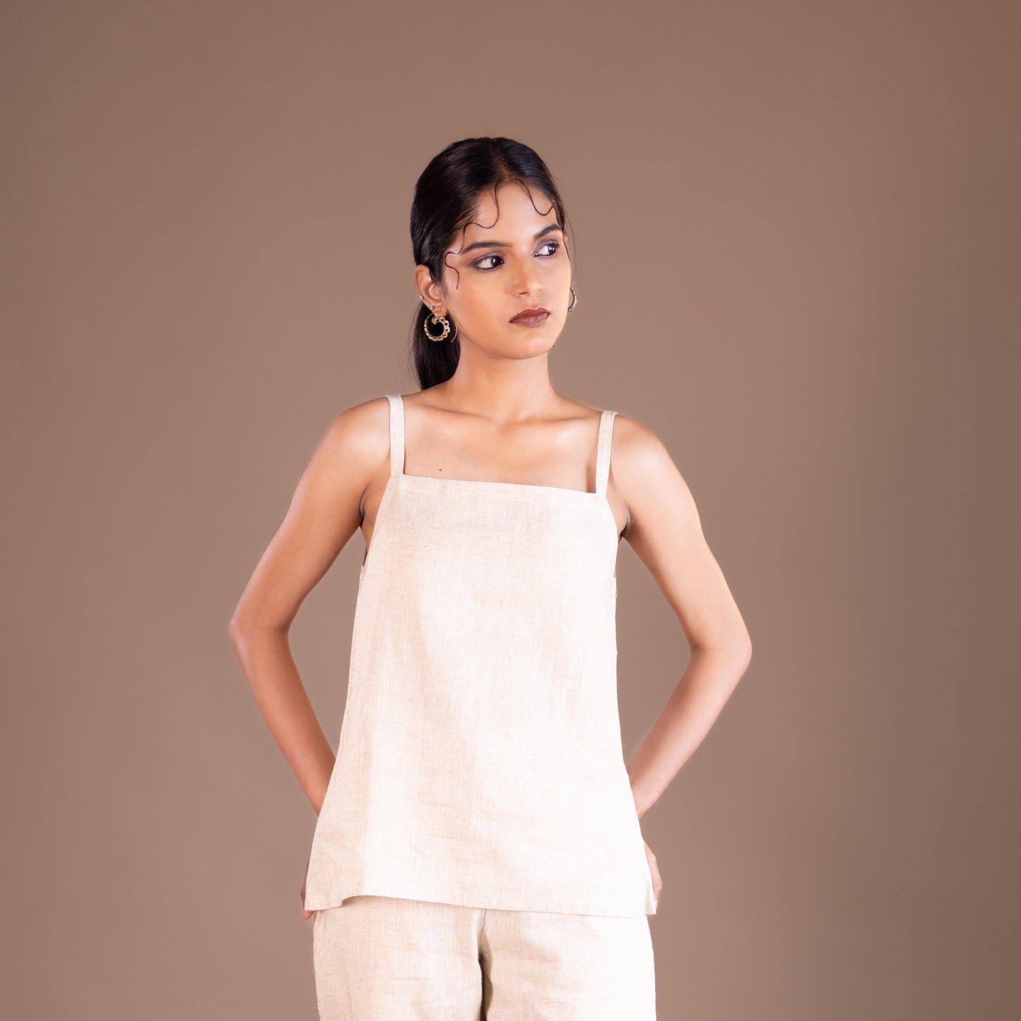Woman wearing a beige top and pants against a brown background