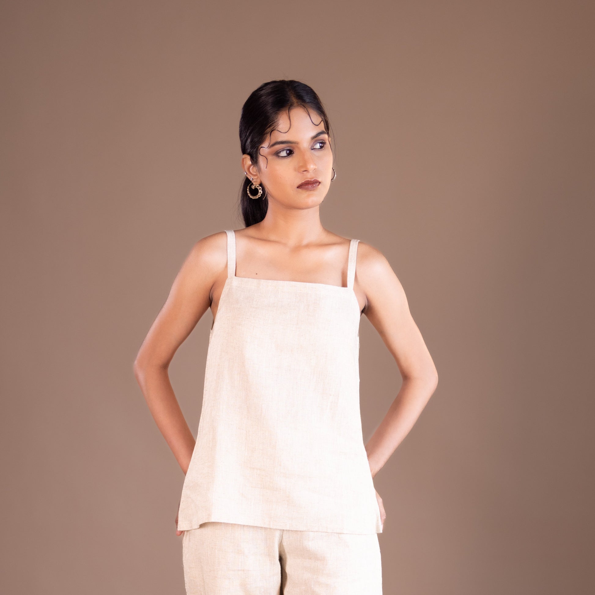 Woman wearing a beige top and pants against a brown background