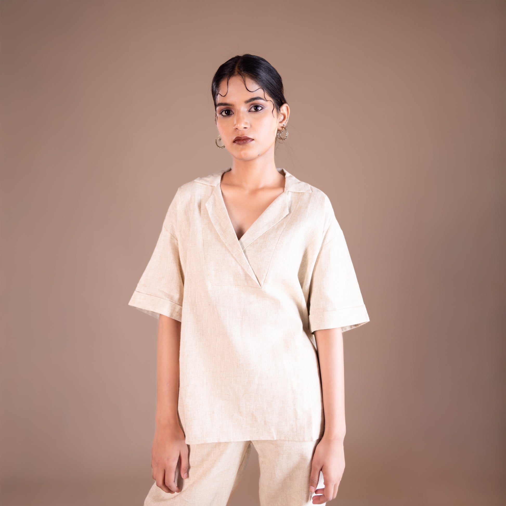 Woman wearing a beige shirt and pants against a brown background