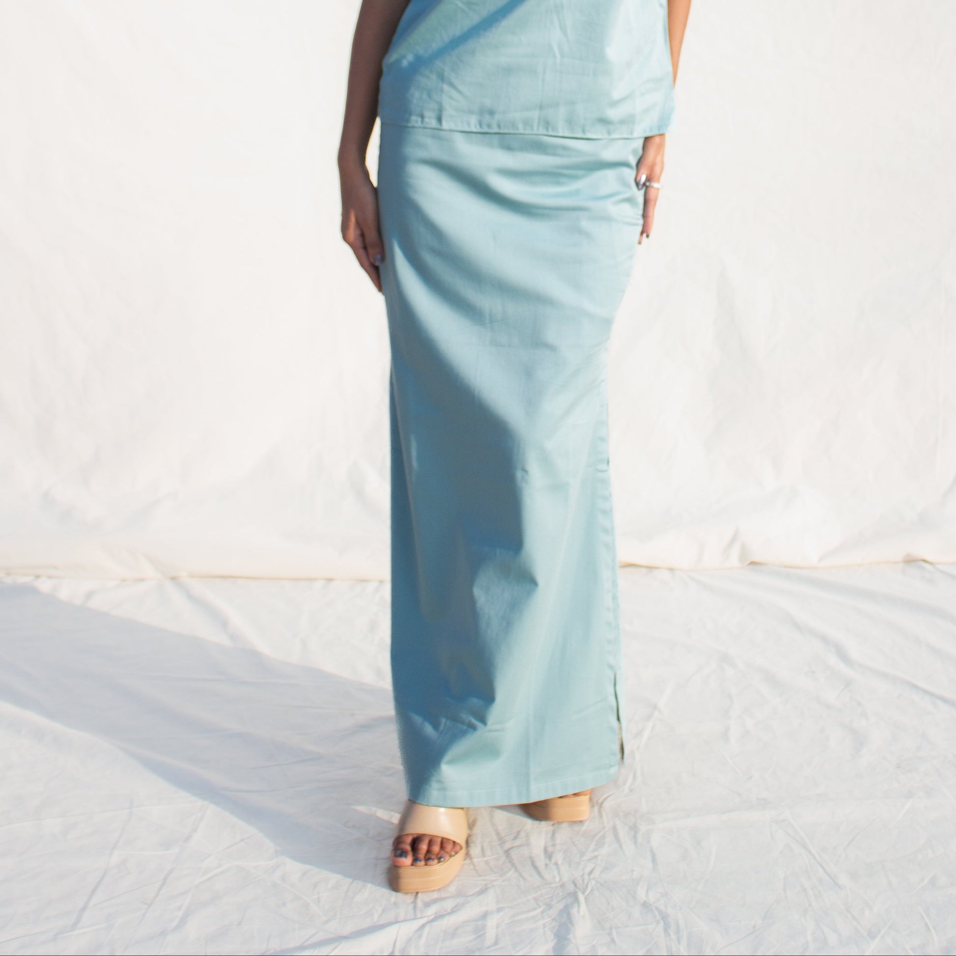 Woman wearing a light blue sleeveless top and pants against a white background
