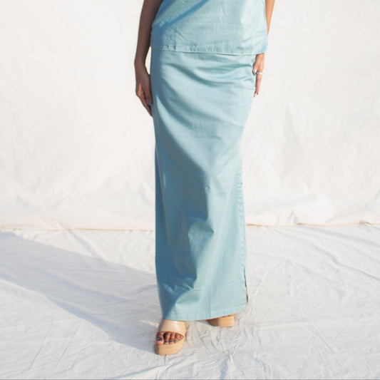 Woman wearing a light blue sleeveless top and pants against a white background