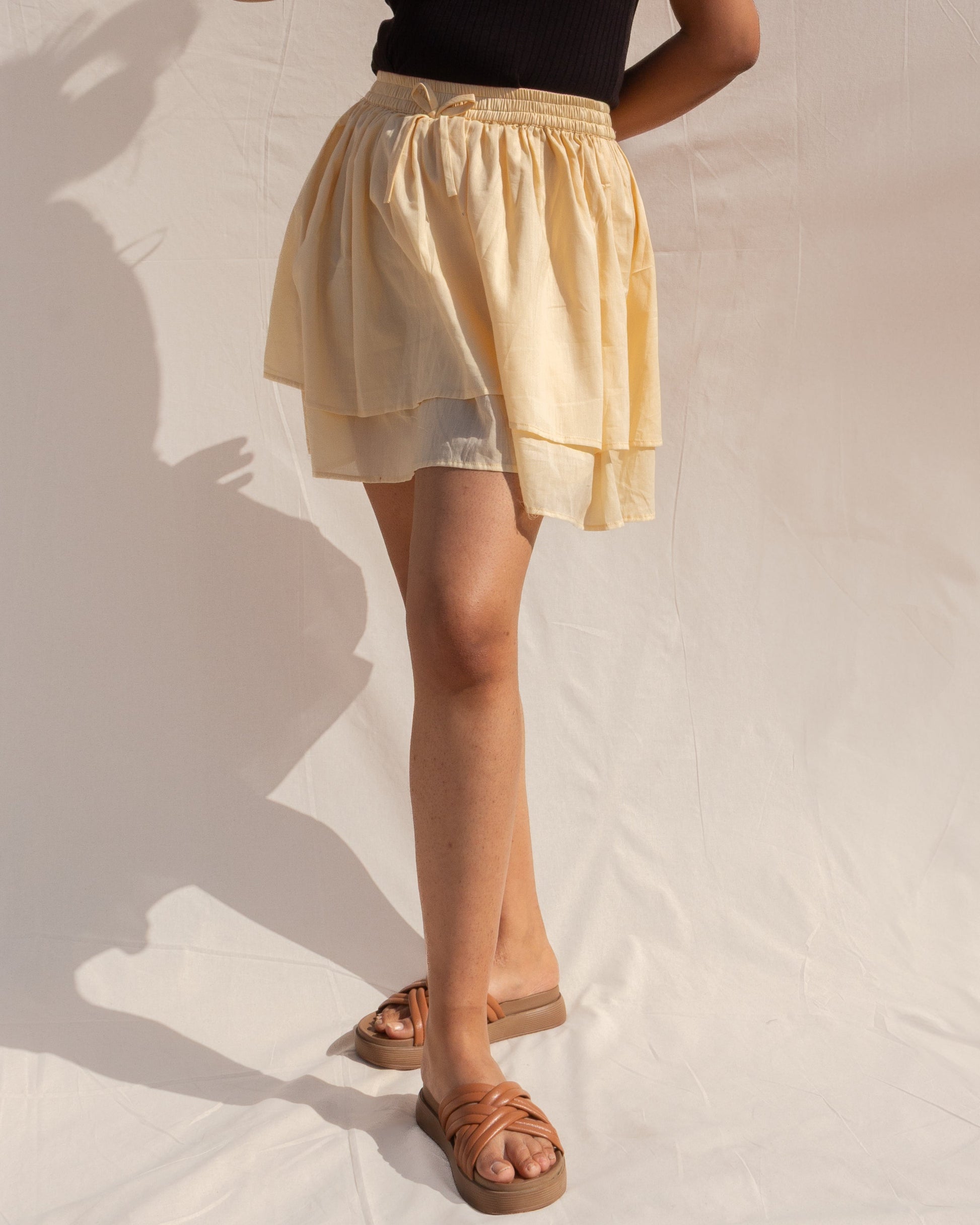 Woman wearing a black top and yellow skirt against a neutral background