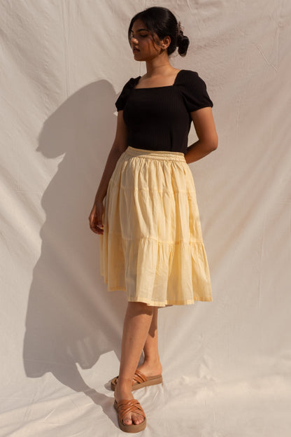 Woman wearing a black top and beige skirt against a plain background