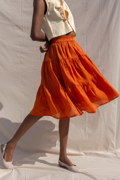 Person wearing a white top and orange skirt against a plain background