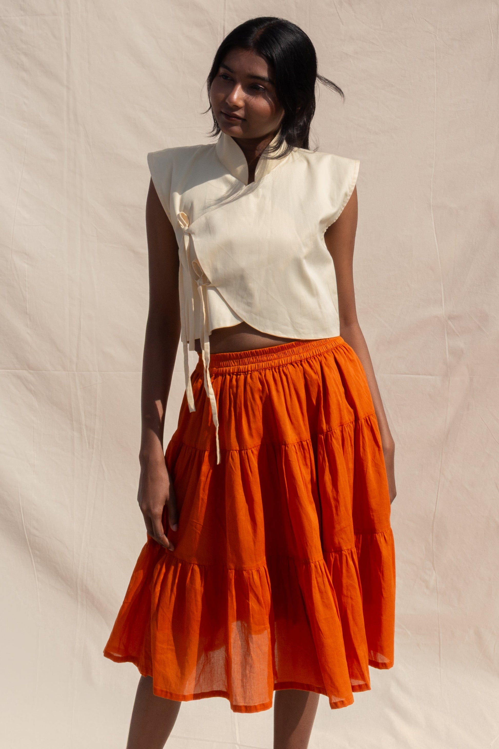 Woman wearing a white top and orange skirt against a beige background