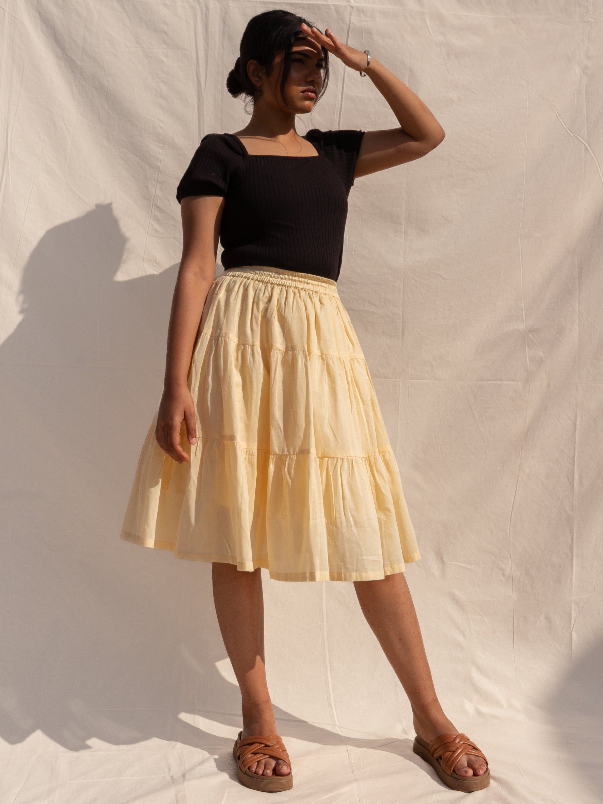 Woman wearing a black top and beige skirt against a plain background