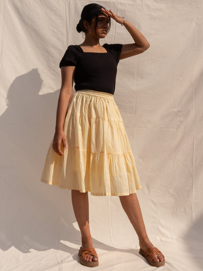 Woman wearing a black top and beige skirt against a plain background