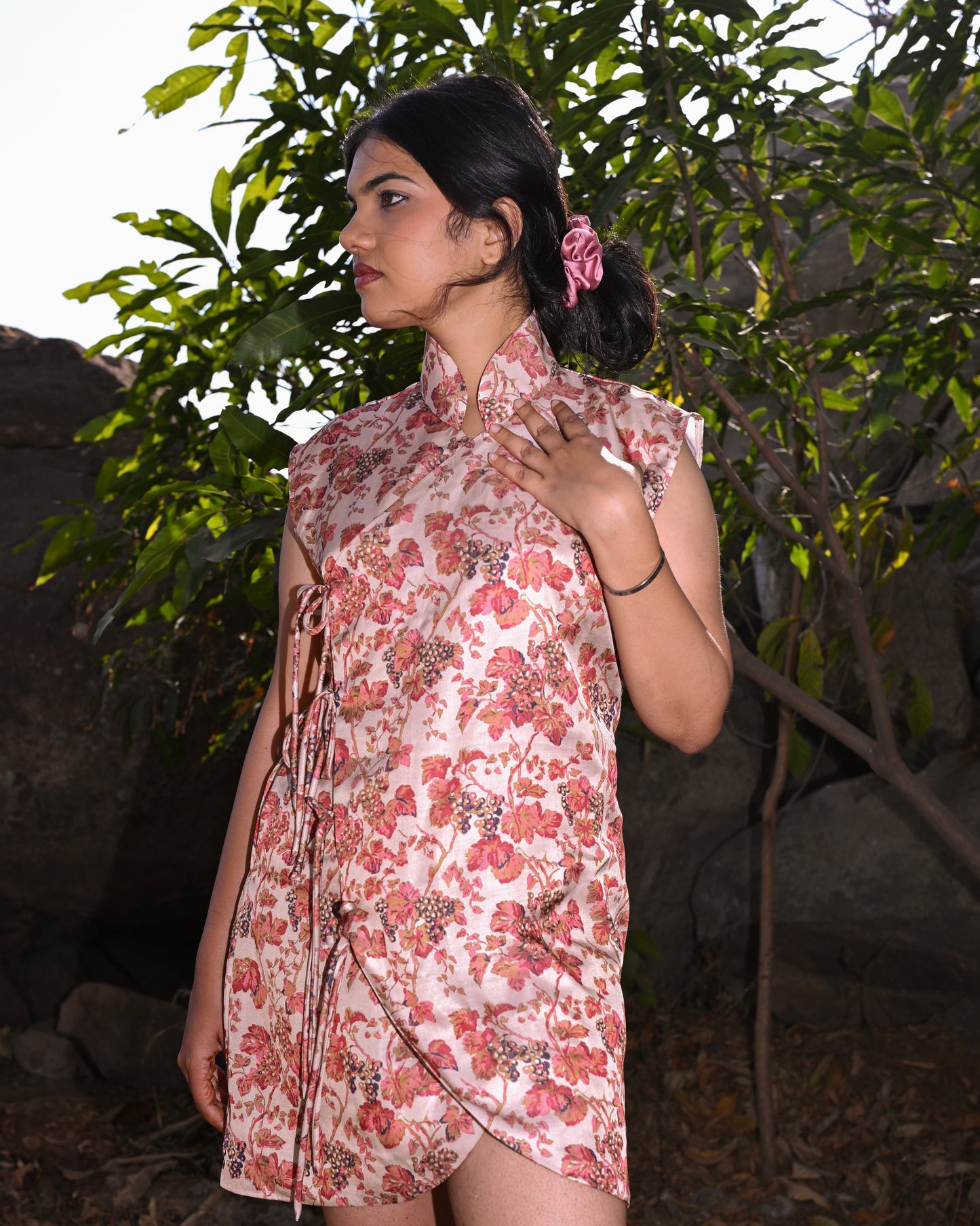 Woman wearing a floral dress standing in a natural setting with greenery.