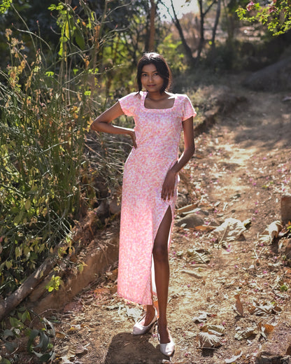 Woman in a pink dress standing on a dirt path with greenery around