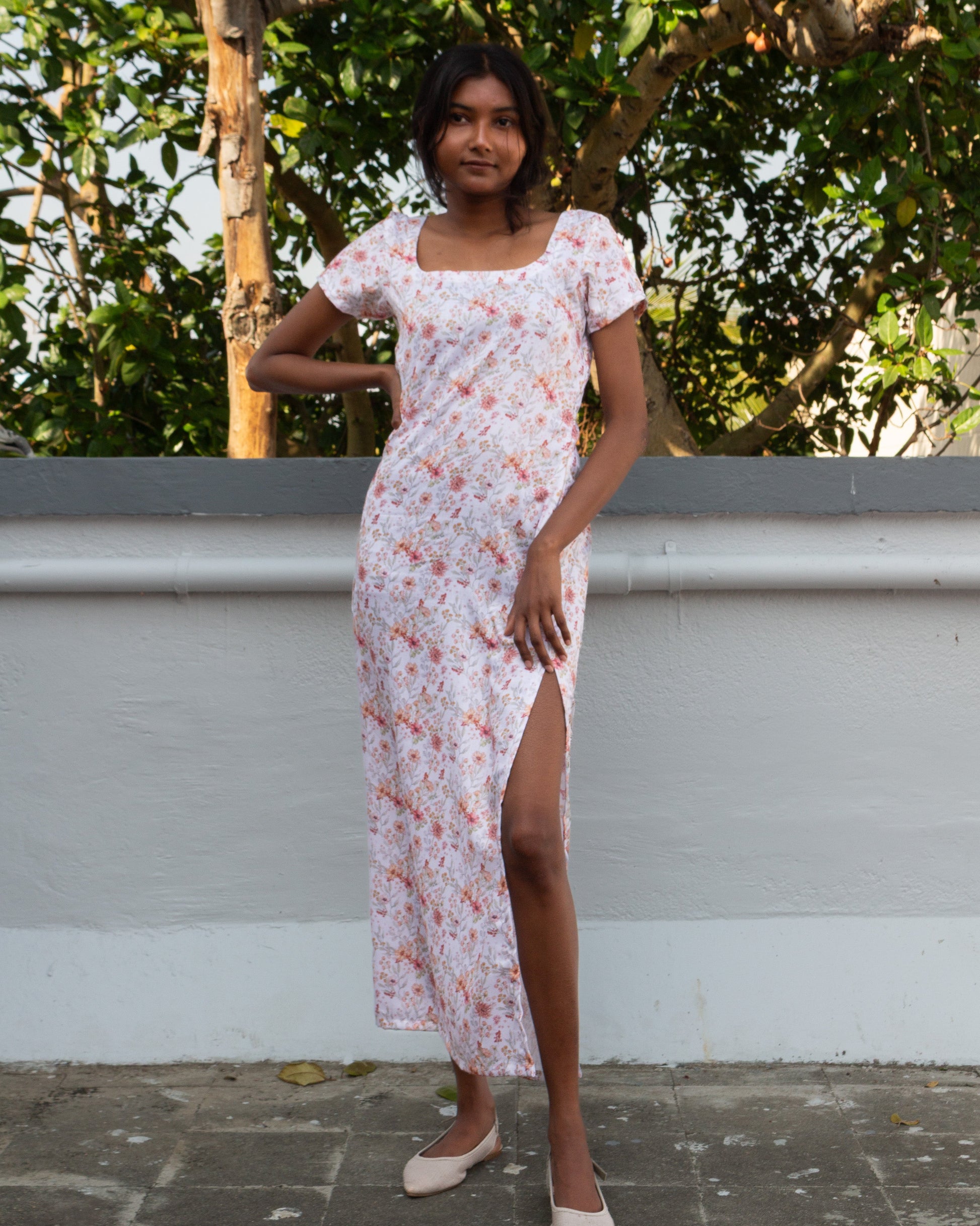 Woman in a floral dress standing outdoors with greenery in the background