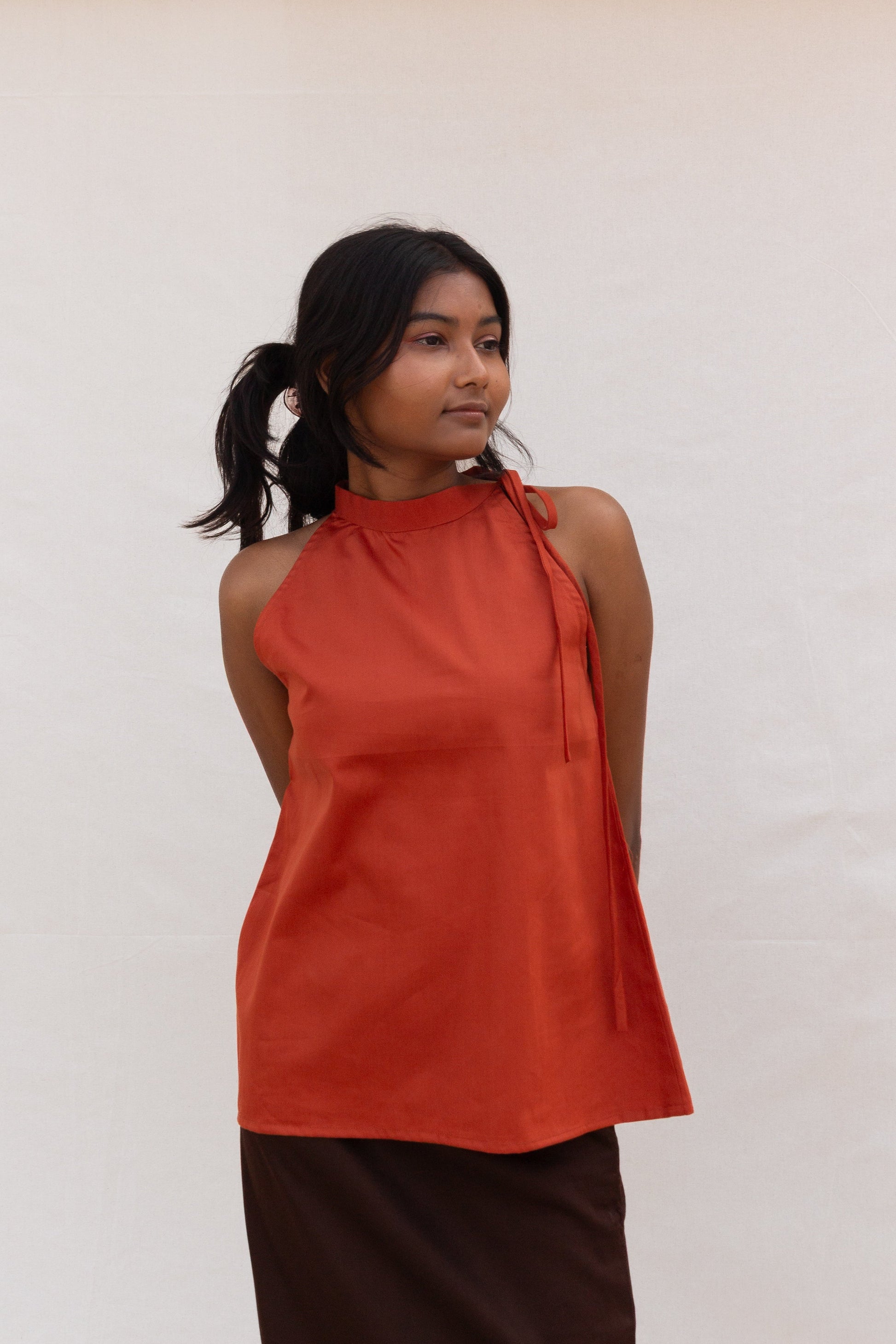 Woman wearing an rust sleeveless top against a white background