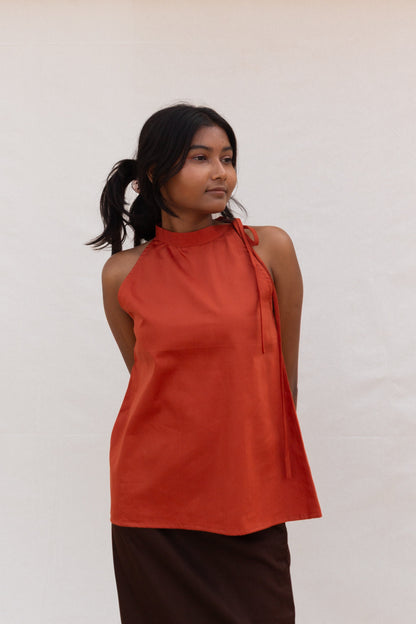Woman wearing an rust sleeveless top against a white background