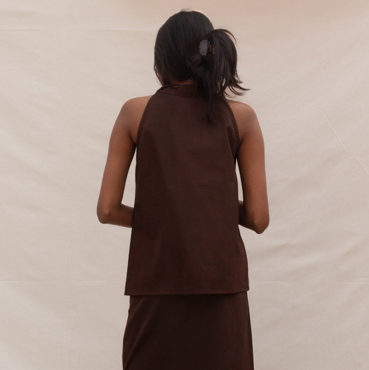 Woman wearing a brown sleeveless top and skirt set on a beige background