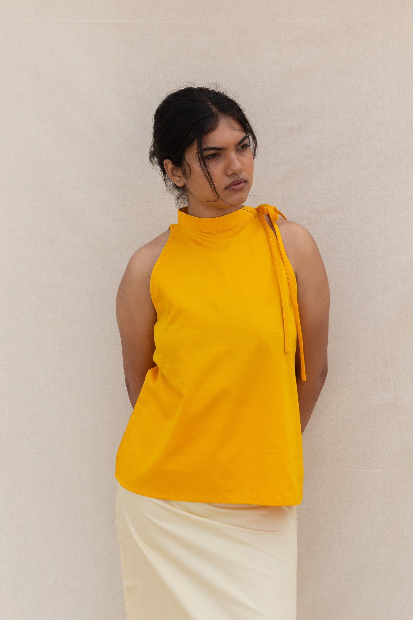 Woman wearing a yellow sleeveless top with a knot detail on a plain background