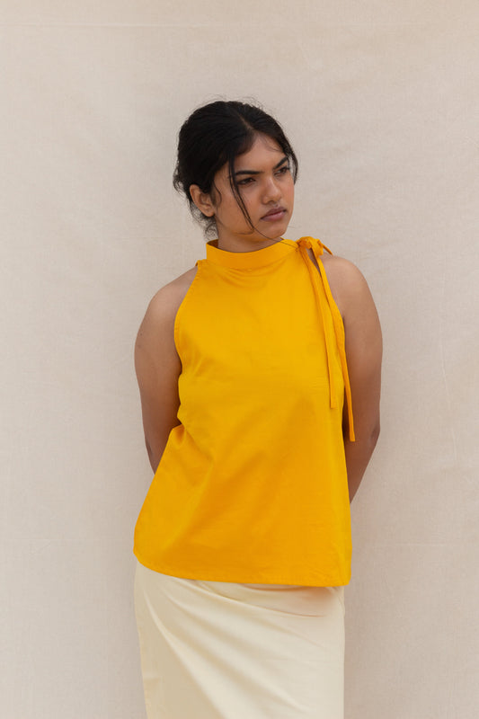 Woman wearing a yellow sleeveless top with a knot detail on a plain background