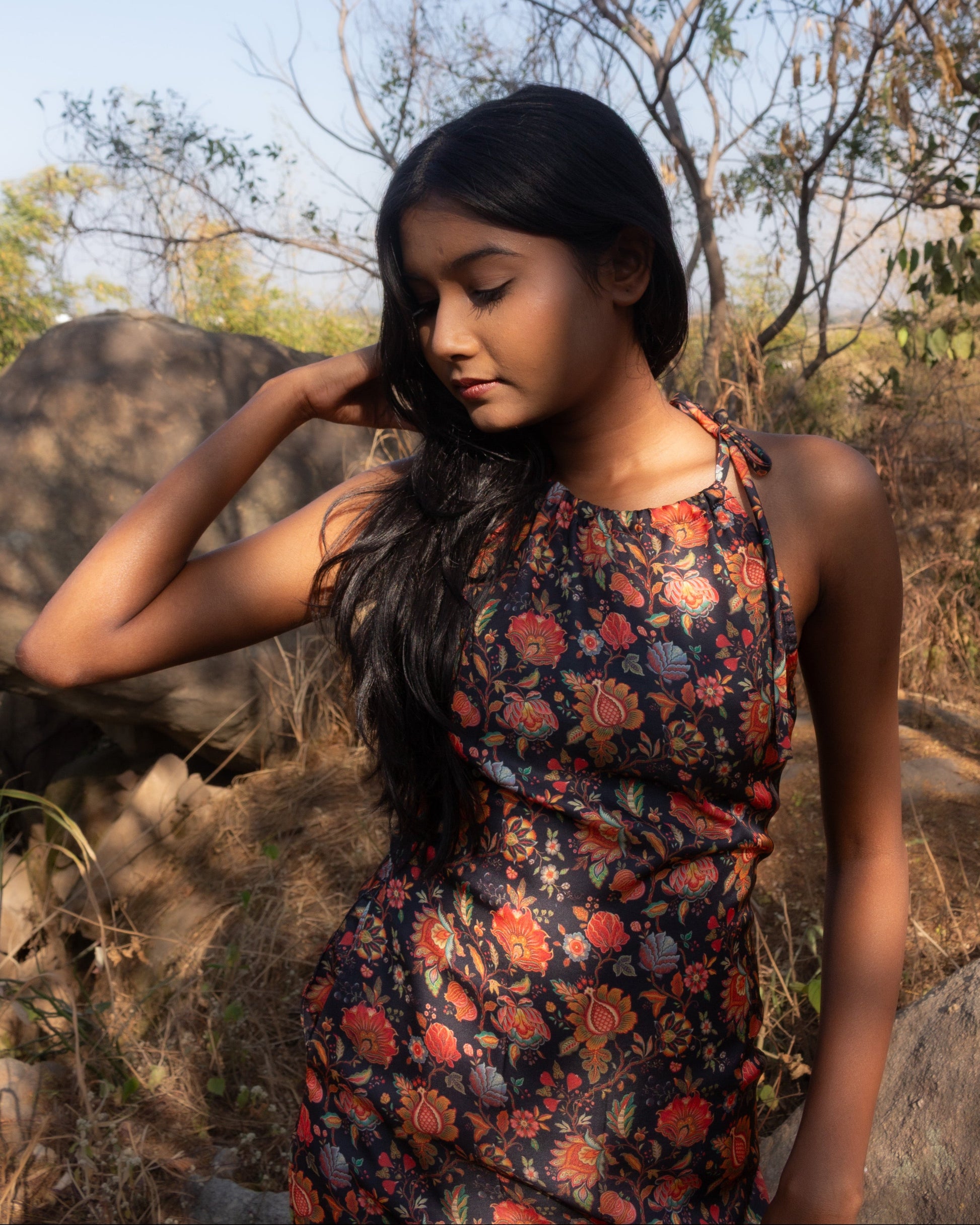 Woman in a floral dress standing outdoors with trees and rocks in the background