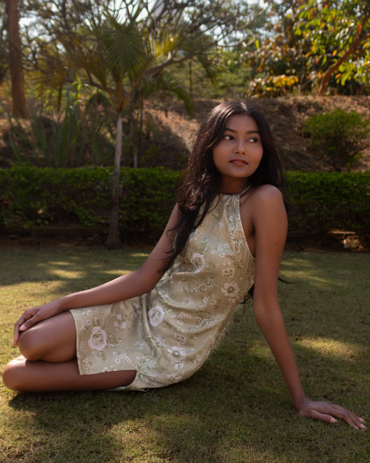 Woman in a patterned dress sitting on grass with trees in the background
