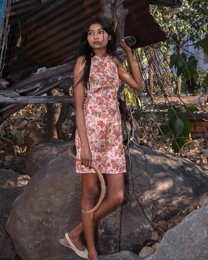 Woman in a floral dress standing outdoors near rustic structures and trees