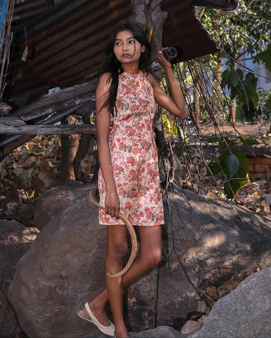 Woman in a floral dress standing outdoors near rustic structures and trees