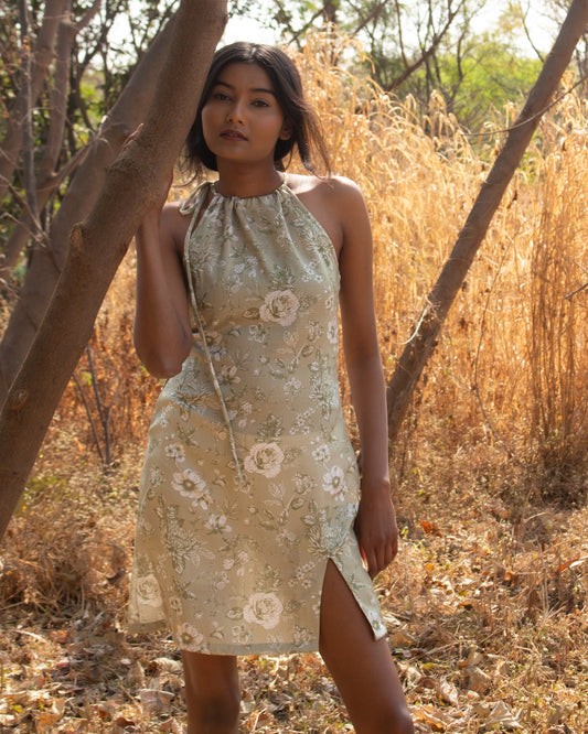 Woman in a floral dress standing in a natural setting with trees and dry grass.