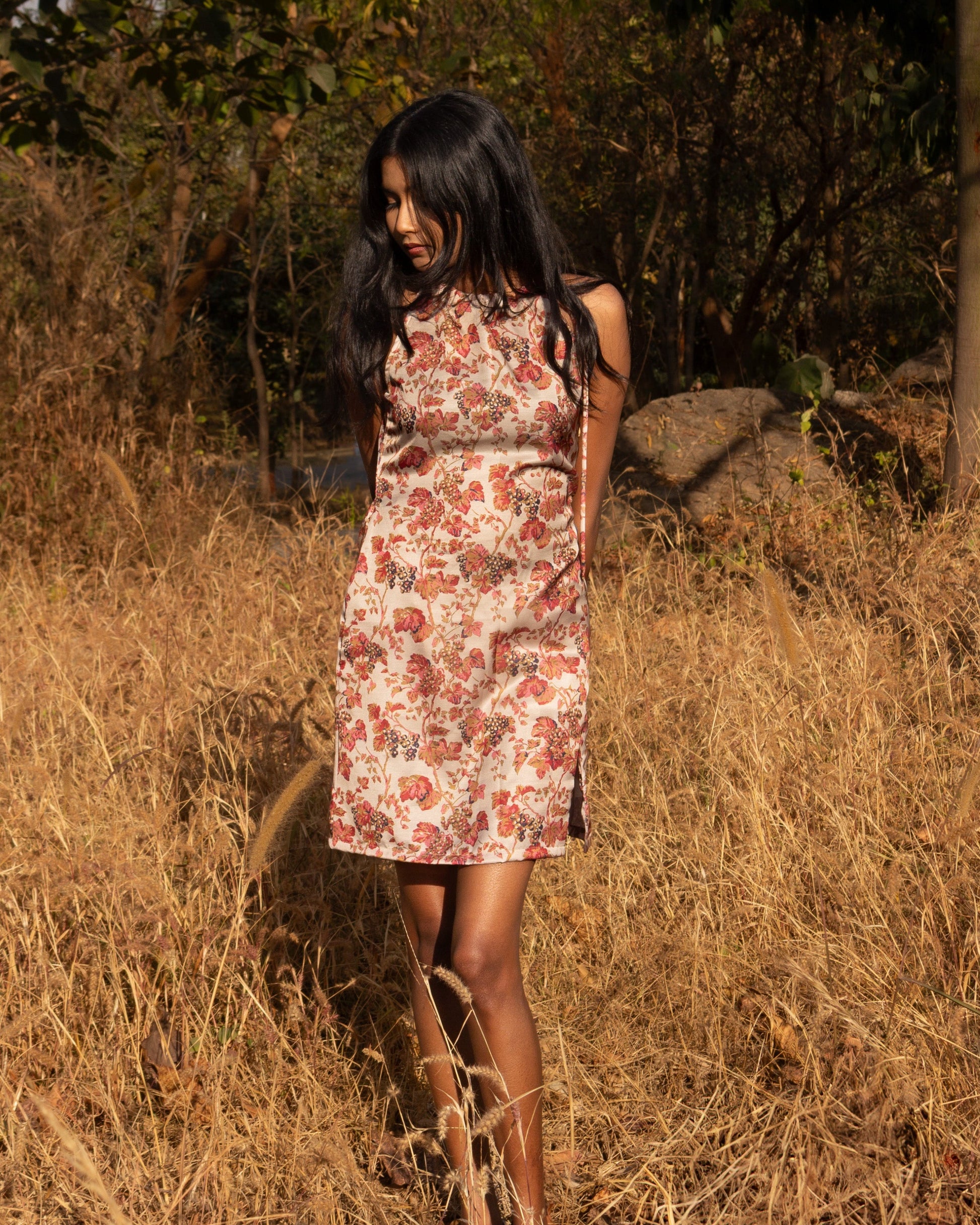 Woman in a floral dress standing in a dry grass field with trees in the background