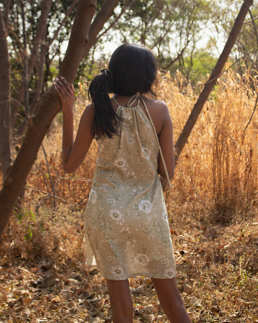 Woman in a floral dress standing in a natural setting with trees and dry grass.