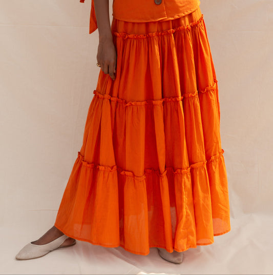Woman wearing an orange outfit with a matching top and tiered skirt against a beige background