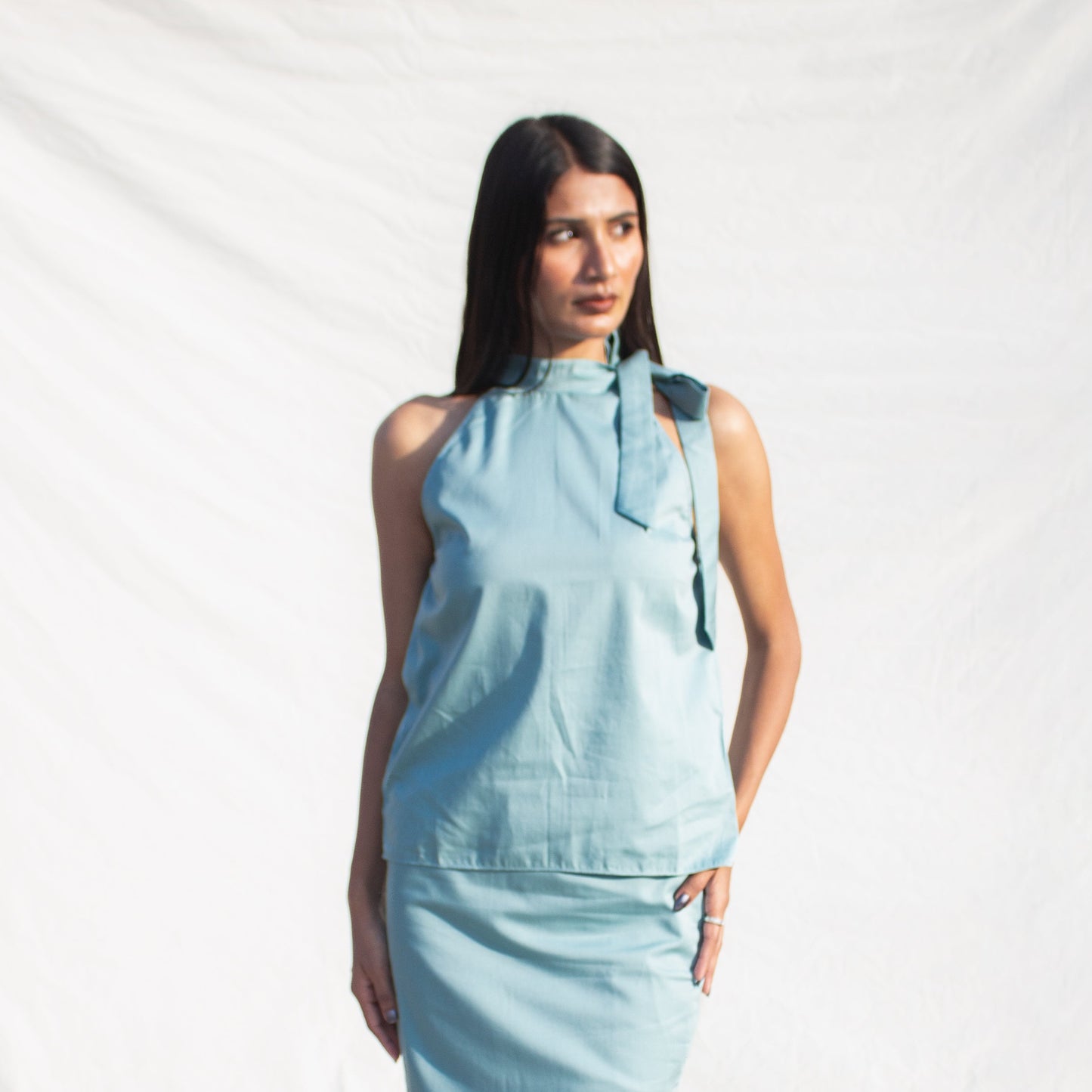 Woman wearing a light blue sleeveless top and pants on a white background