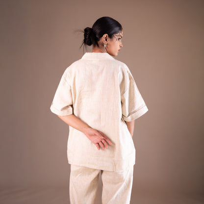 Person wearing a beige outfit against a brown background