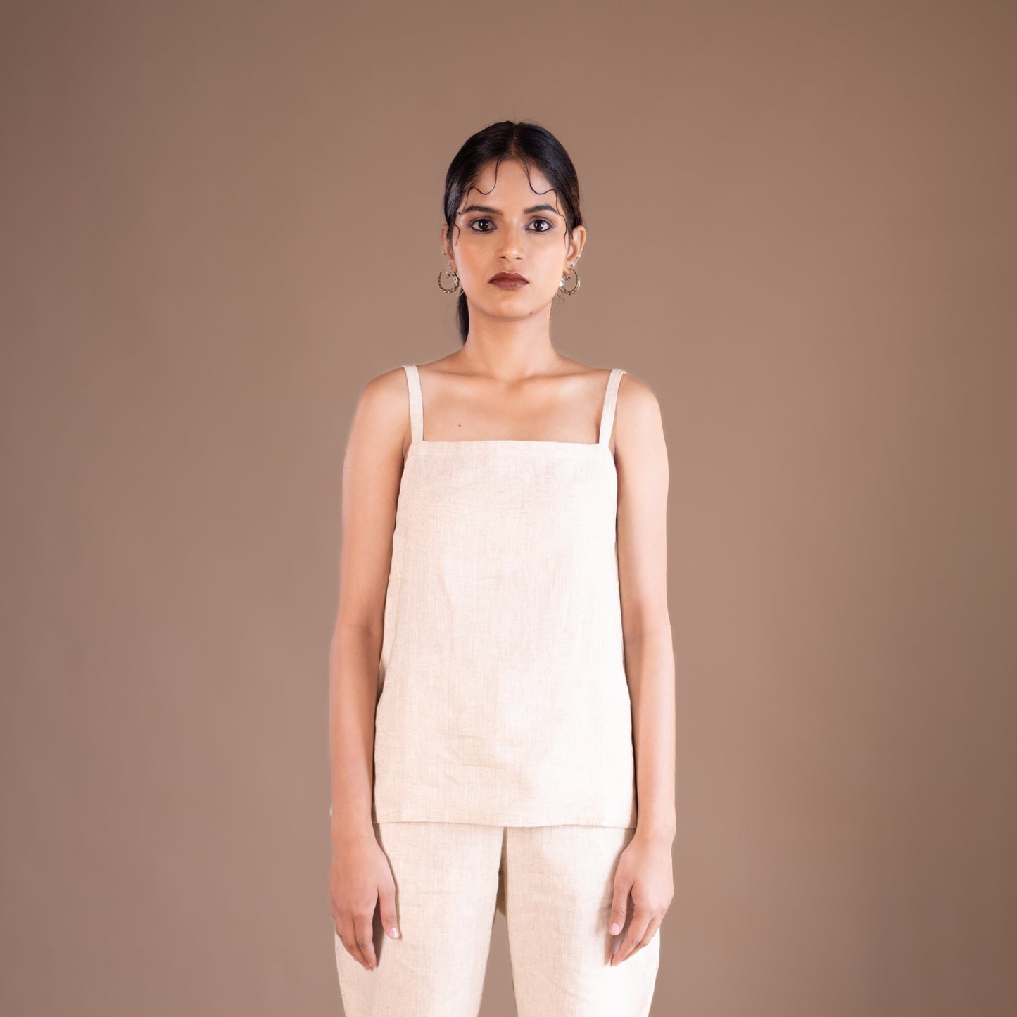 Woman wearing a beige sleeveless top and pants against a brown background