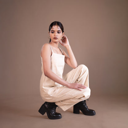 Woman in a beige dress and black boots posing against a brown background