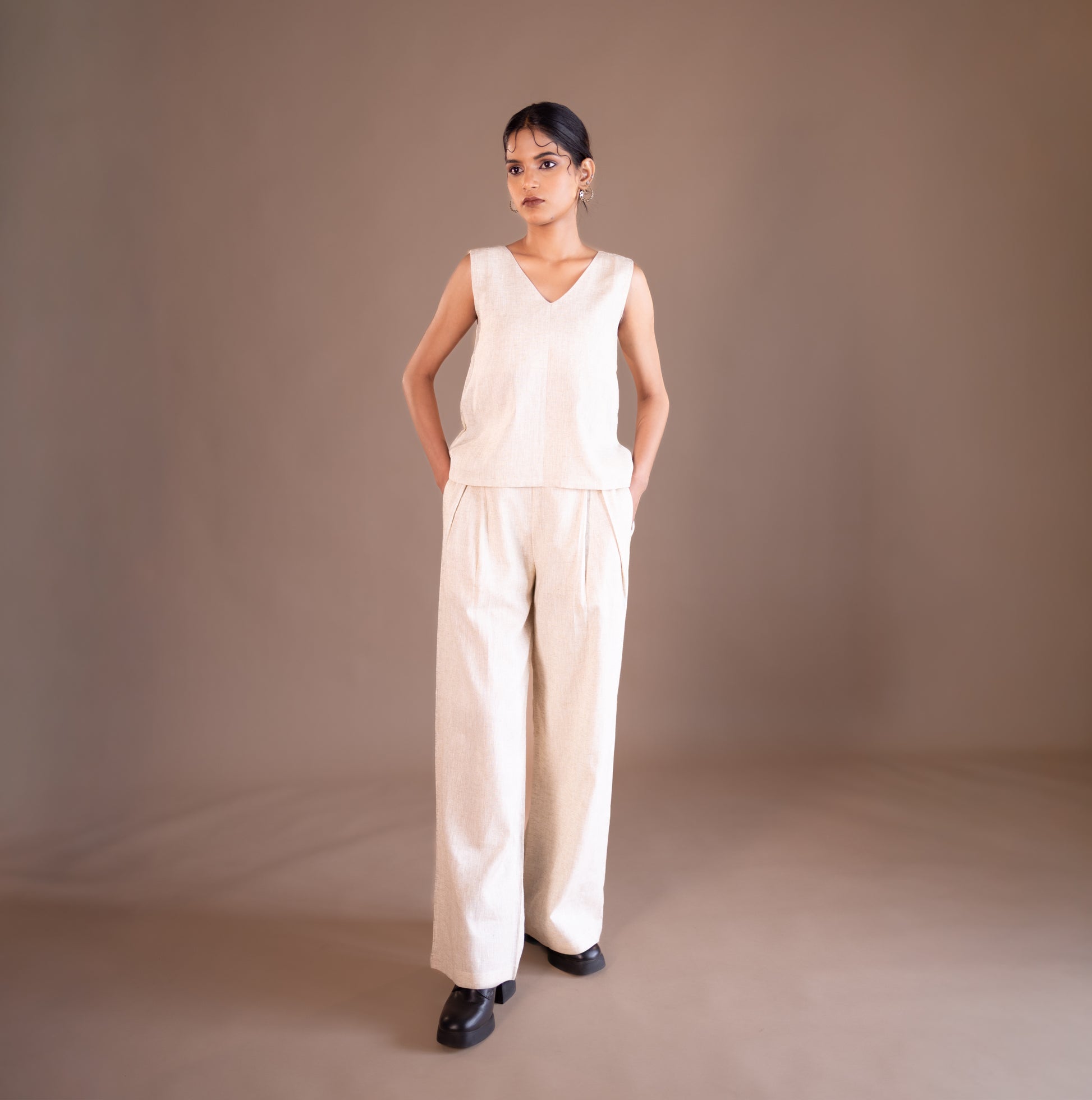 Woman wearing a beige jumpsuit against a brown background