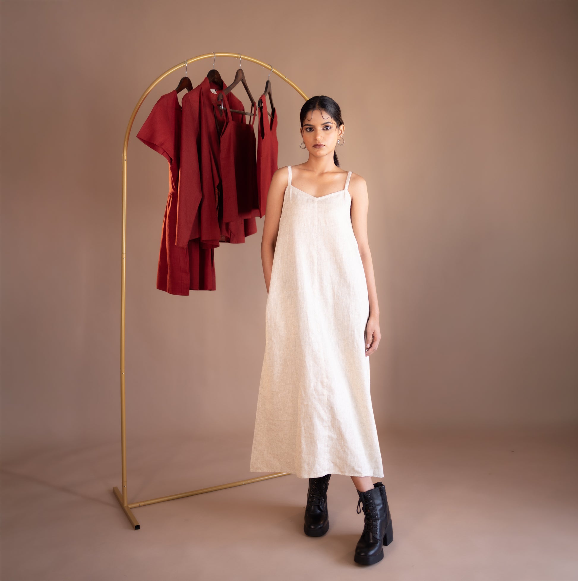 Woman in a beige dress standing next to a gold clothing rack with red garments on a beige background