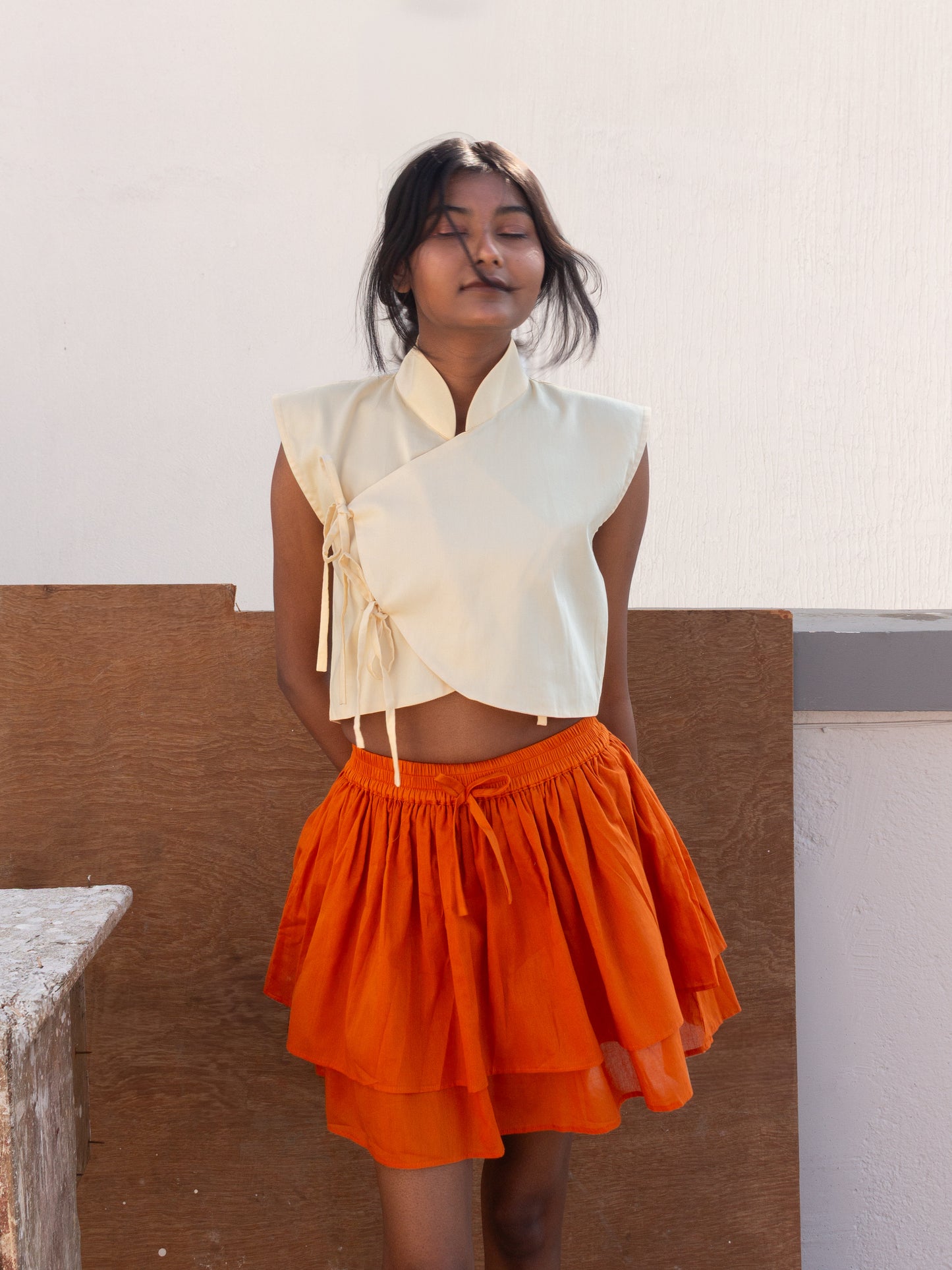Woman wearing a white top and orange skirt against a neutral background