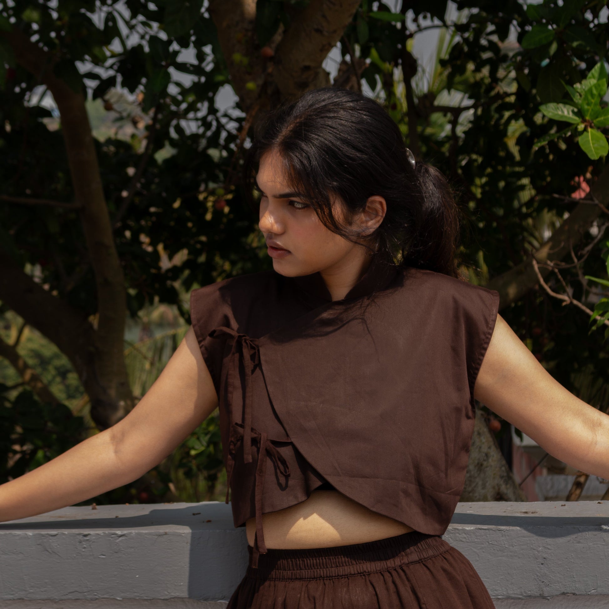 Woman wearing a brown outfit standing outdoors with greenery in the background